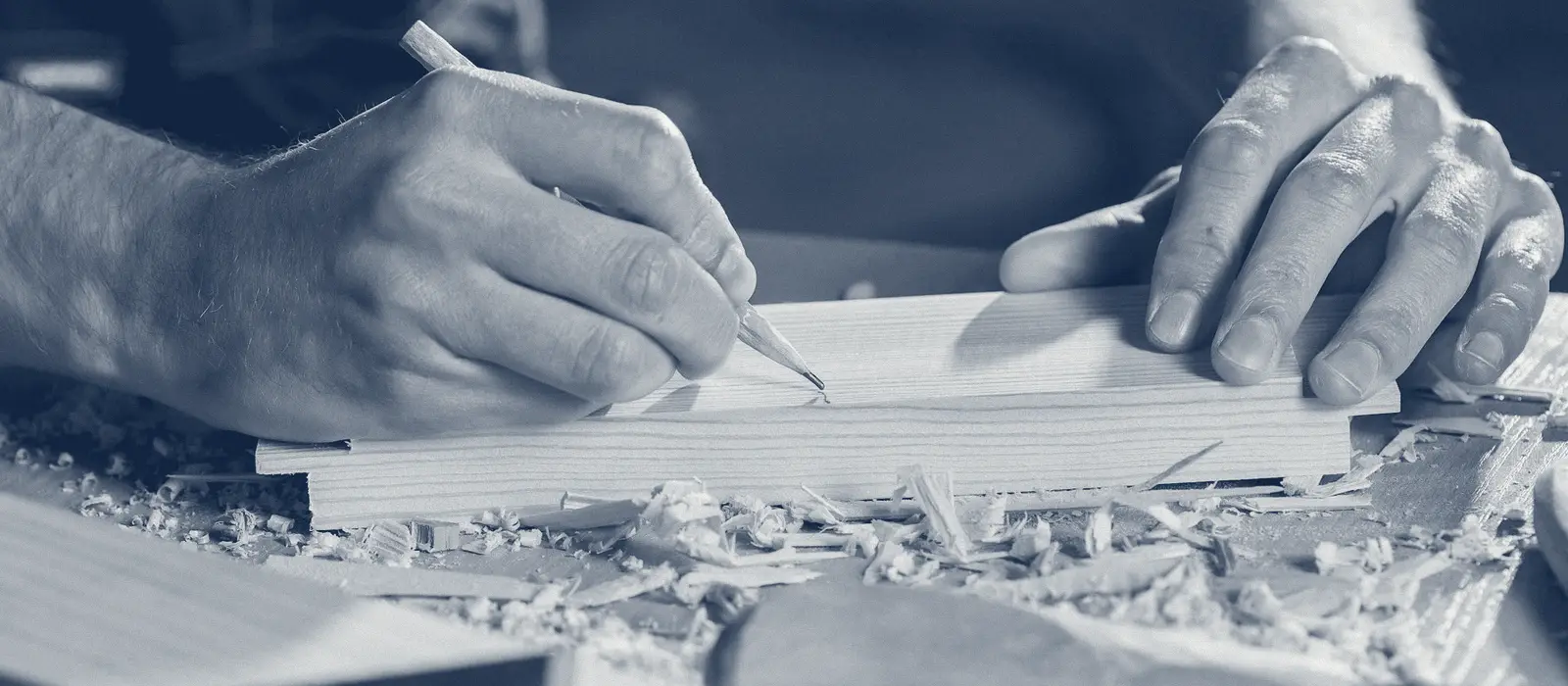 Gros plan sur les mains d'un menuisier qui trace un repère au crayon sur une planche, au milieu des copeaux